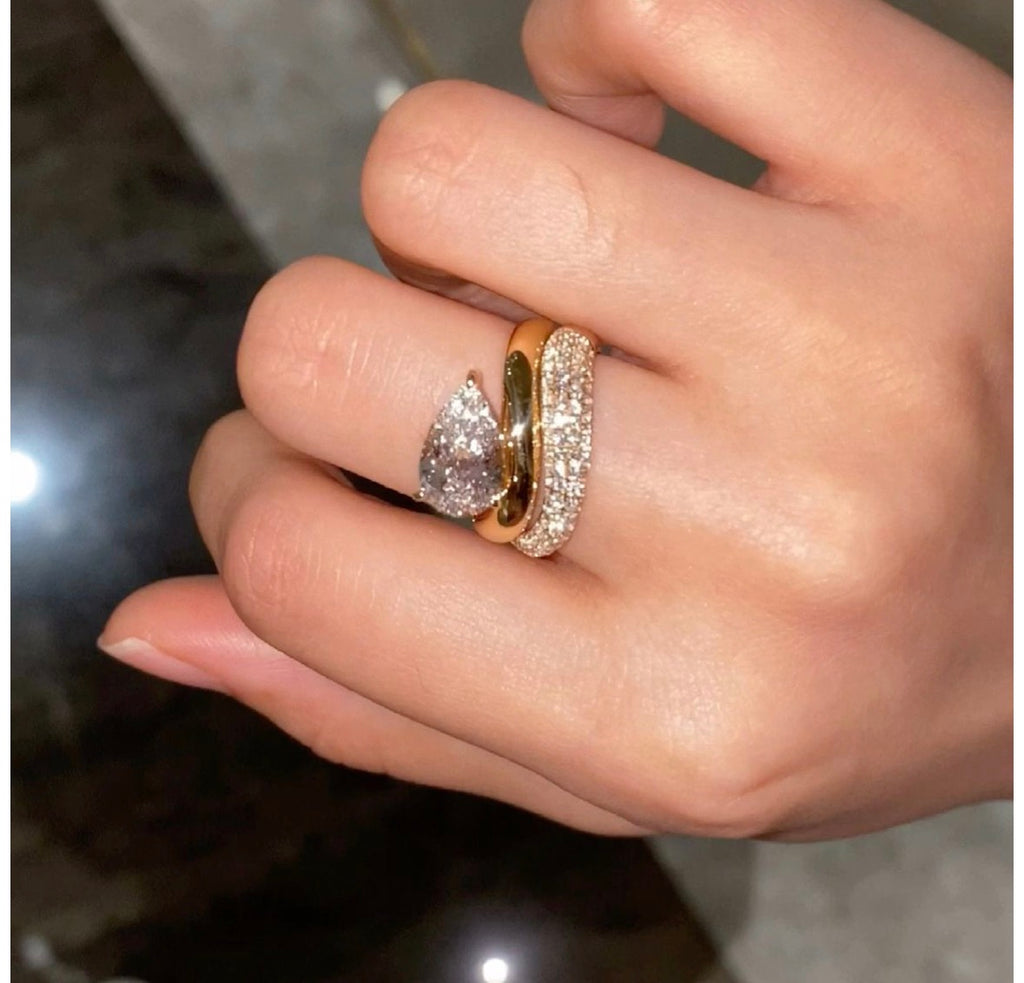 SVAJ diamantring fra Stensgaard med stor pæreformet diamant og skulpturelt guldbånd, vist på hånden sammen med en pavéring.